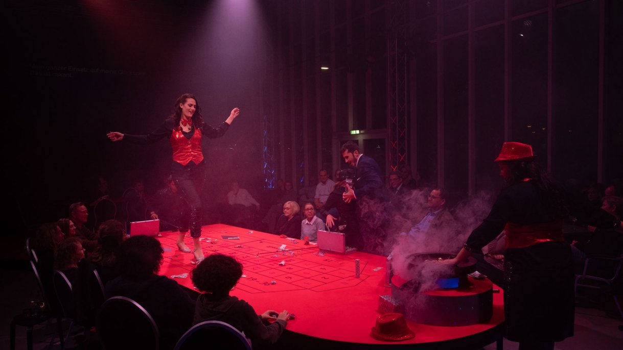 Violetta tanzt auf dem Roulette Tisch, an dem Gäste sitzen 