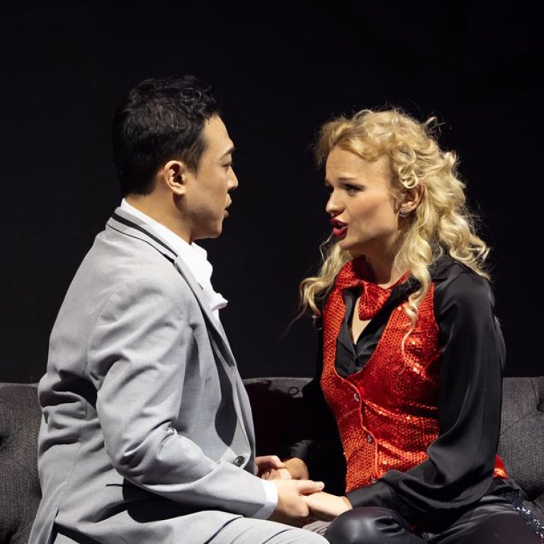 Alfredo und Violetta sitzen sich gegenüber auf dem Sofa