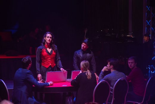 Violetta steht am Poker Tisch, an dem Zuschauer*innen sitzen