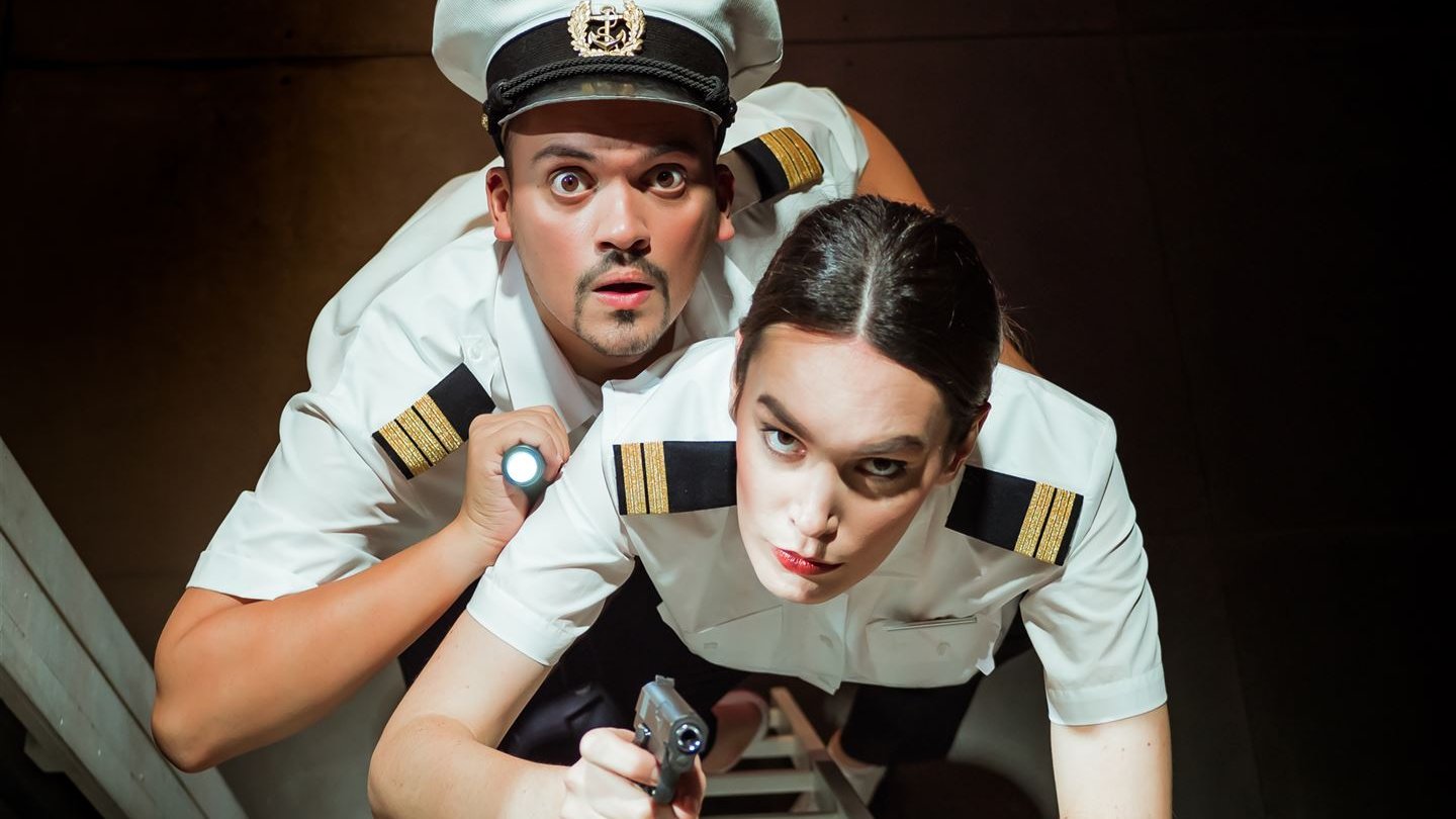 Sängerin und Sänger als Offiziere gekleidet blicken eine Leiter hinauf